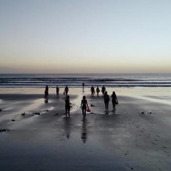 a group of female figures in silhouette on a twilit beach at low tide